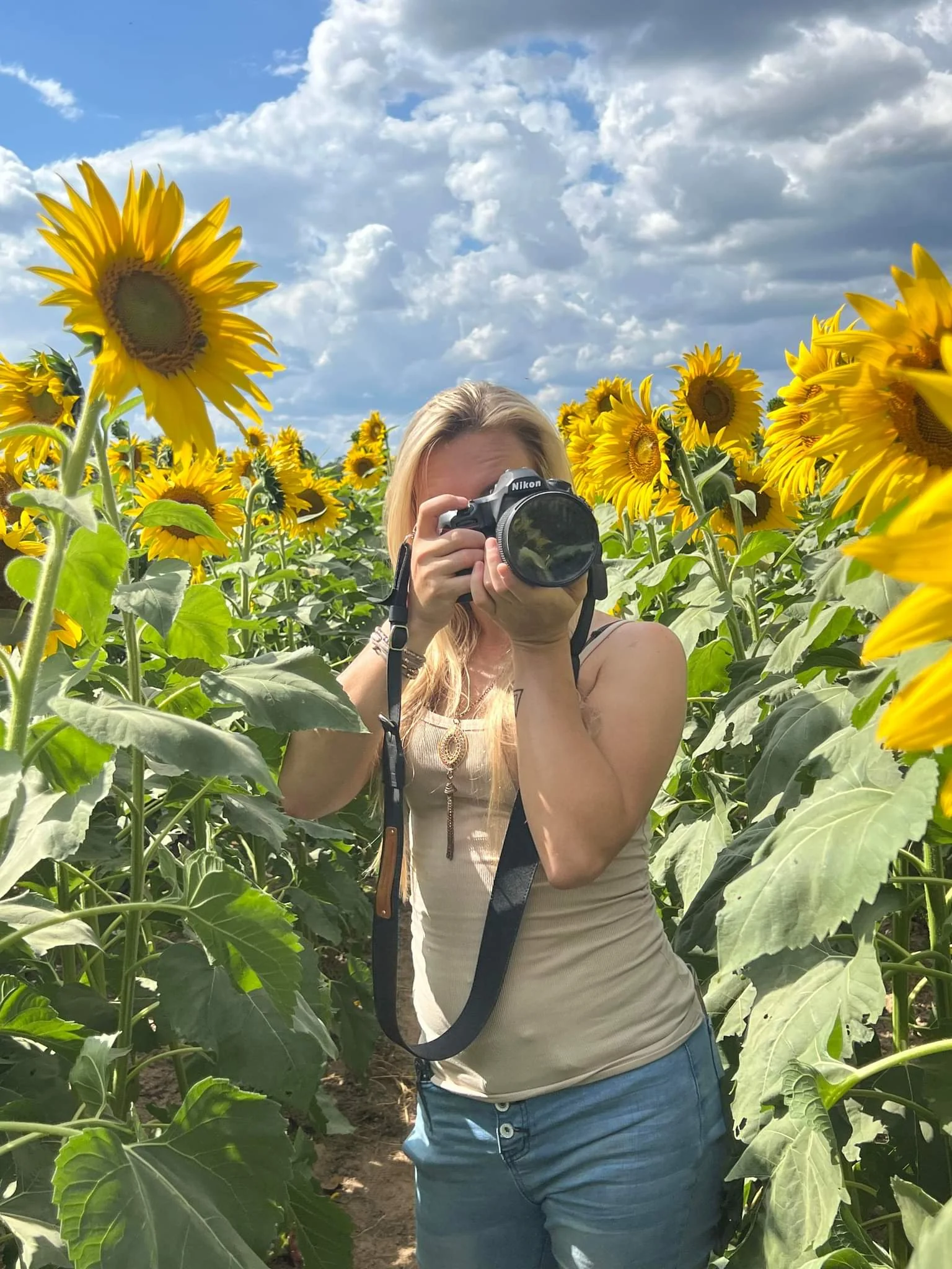 Ashley holding her camera among sunflowers.