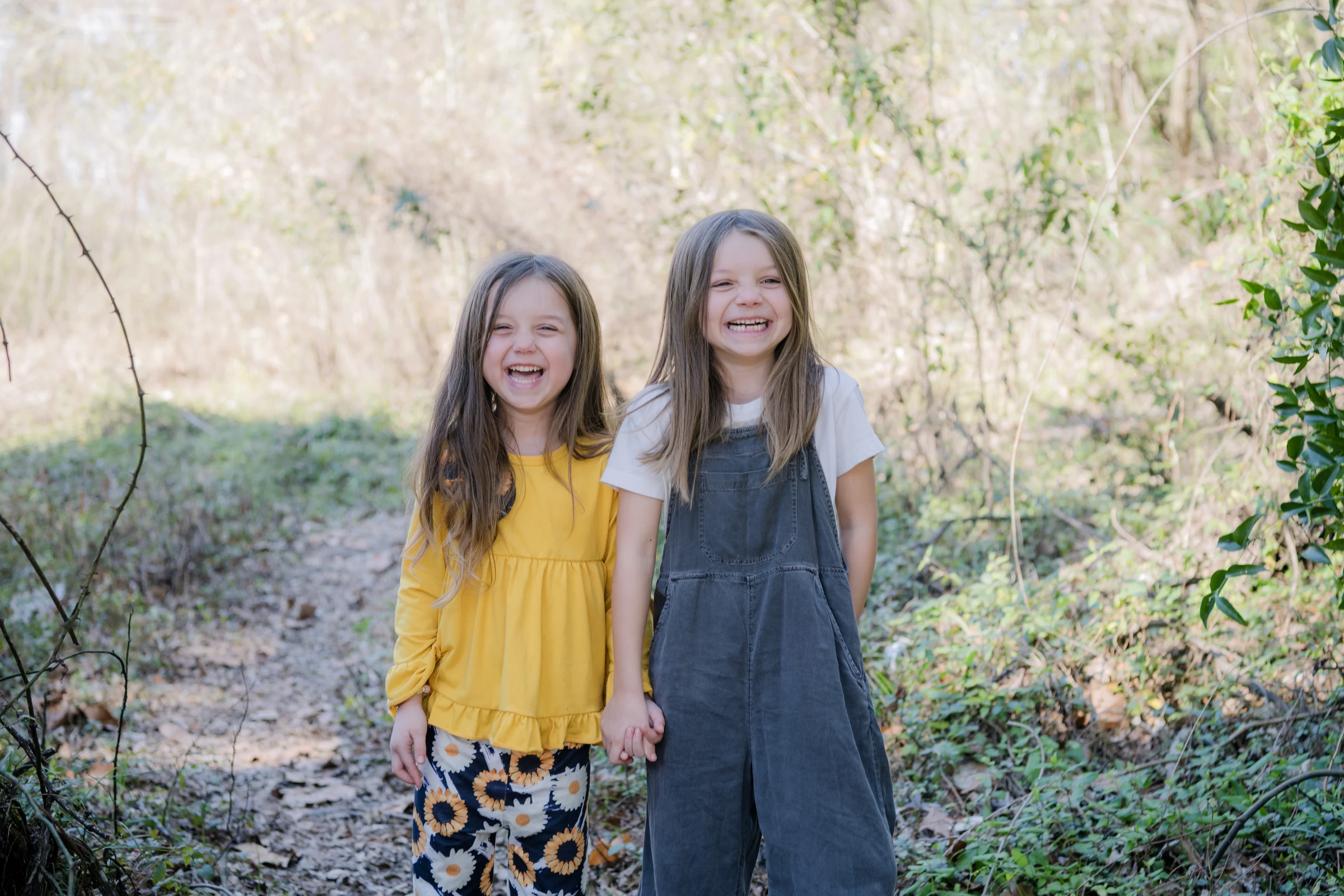 Two children laughing together in a wooded setting.