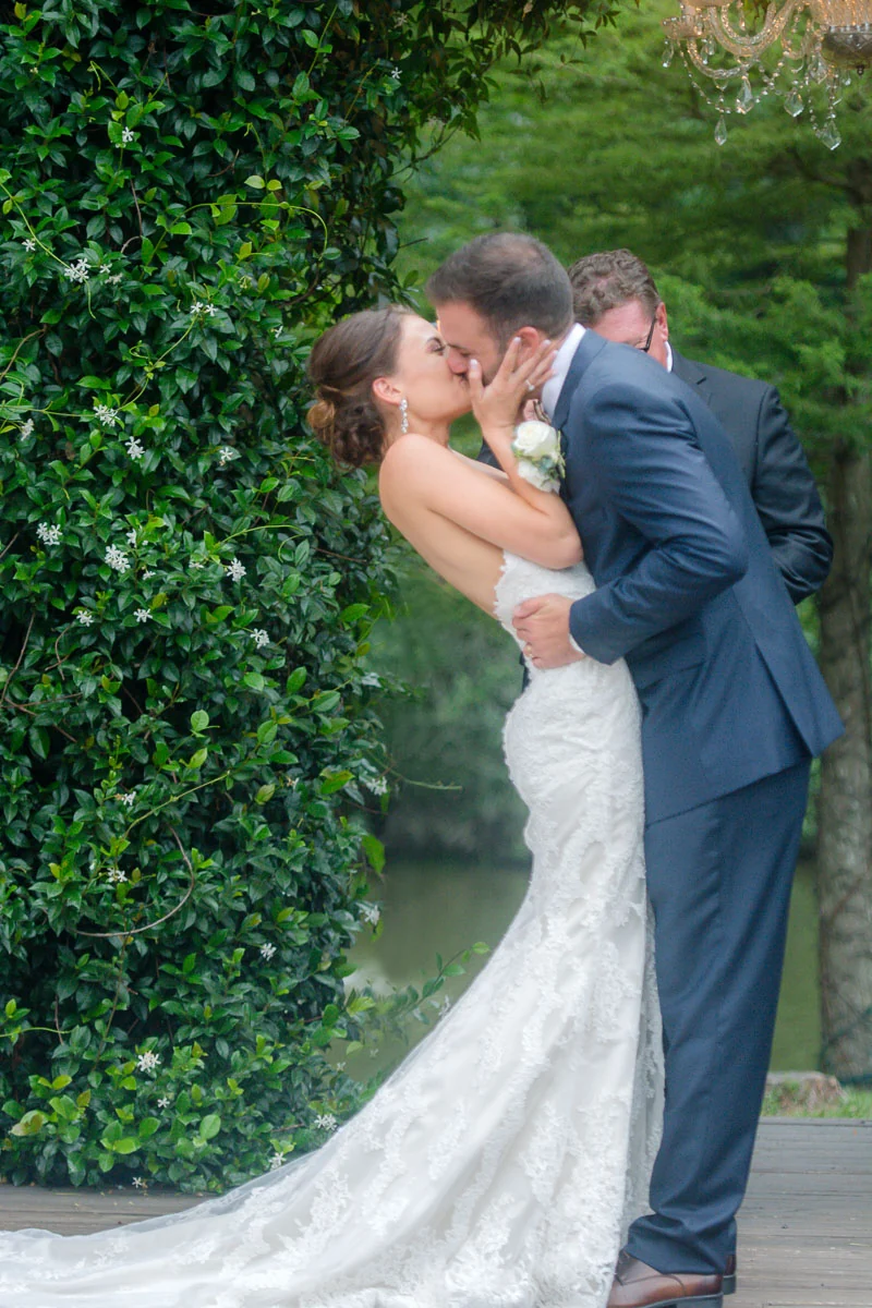 Newlyweds sharing their first kiss beneath greenery and a chandelier.